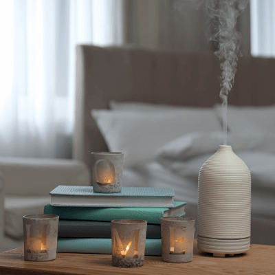 Aroma oil diffuser, candles and books on wooden table in bedroom